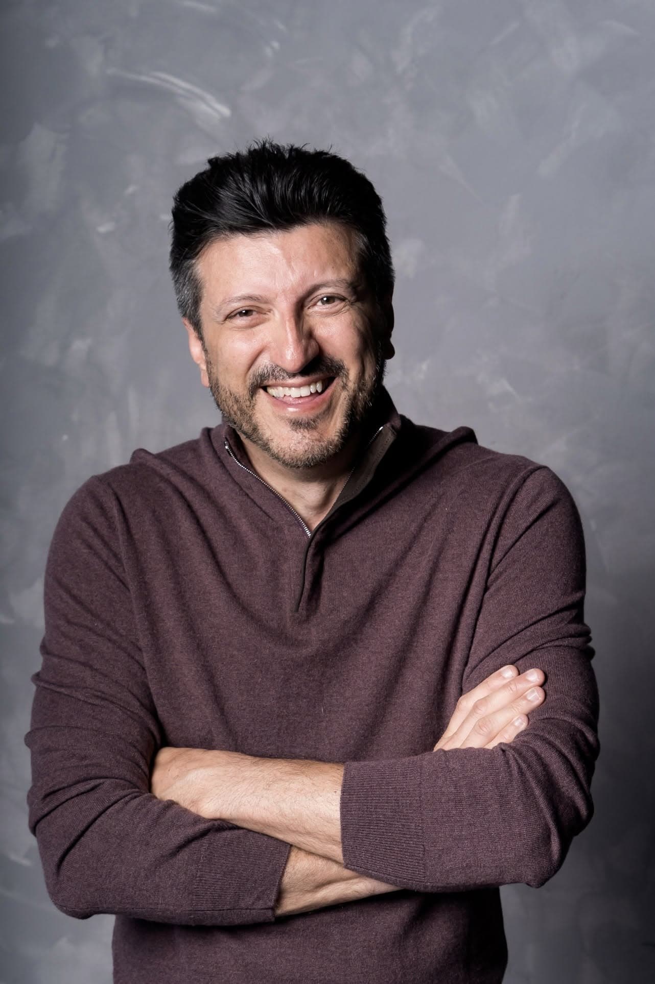 Portrait of Lito Sousa, smiling, arms crossed, wearing a dark sweater.